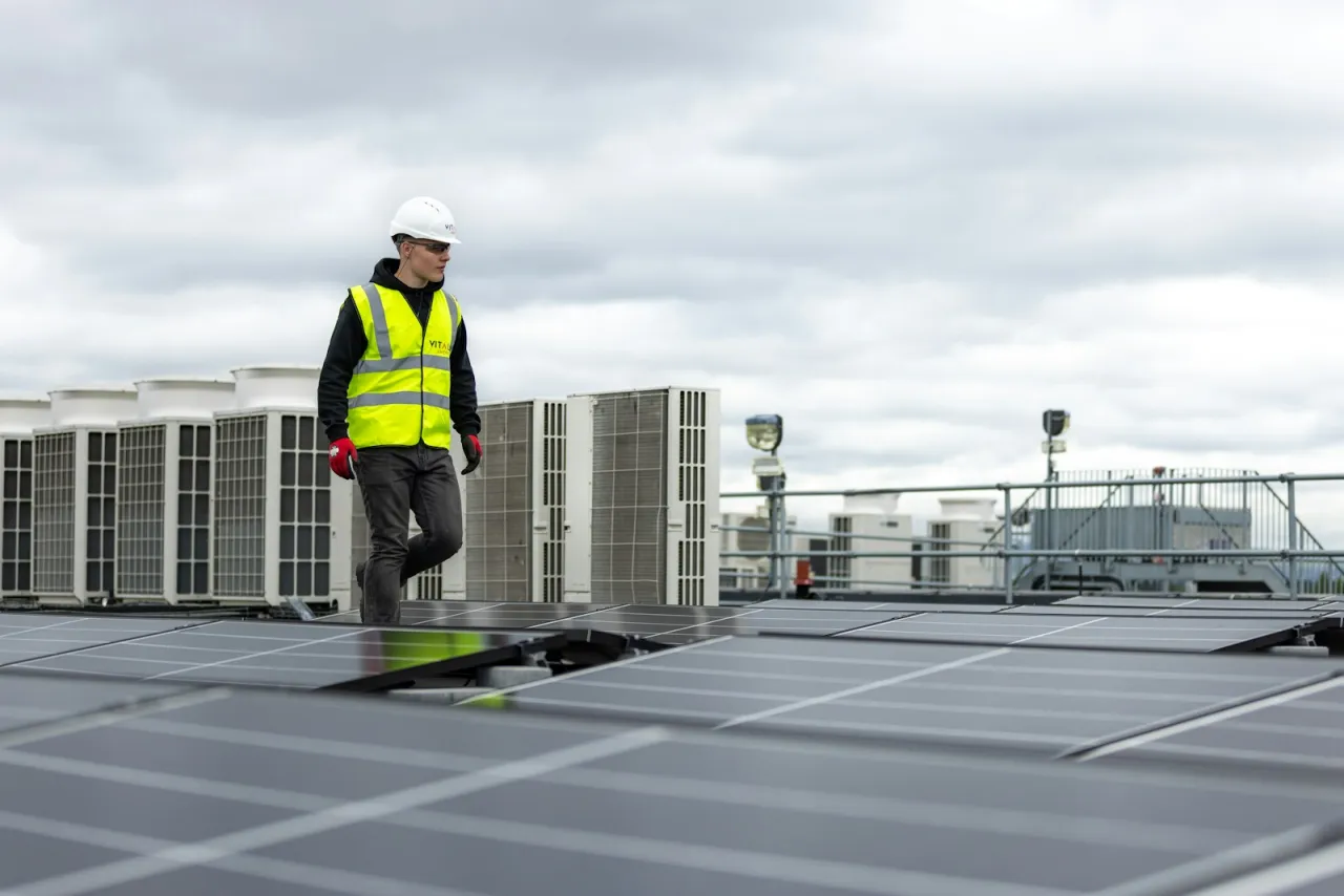 HVAC technician in hi-vis walking across a commercial rooftop past condenser units